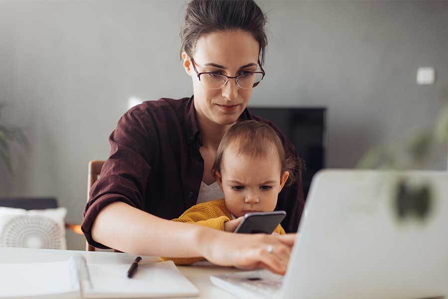 A mother cradling her infant while sitting in front of a laptop computer