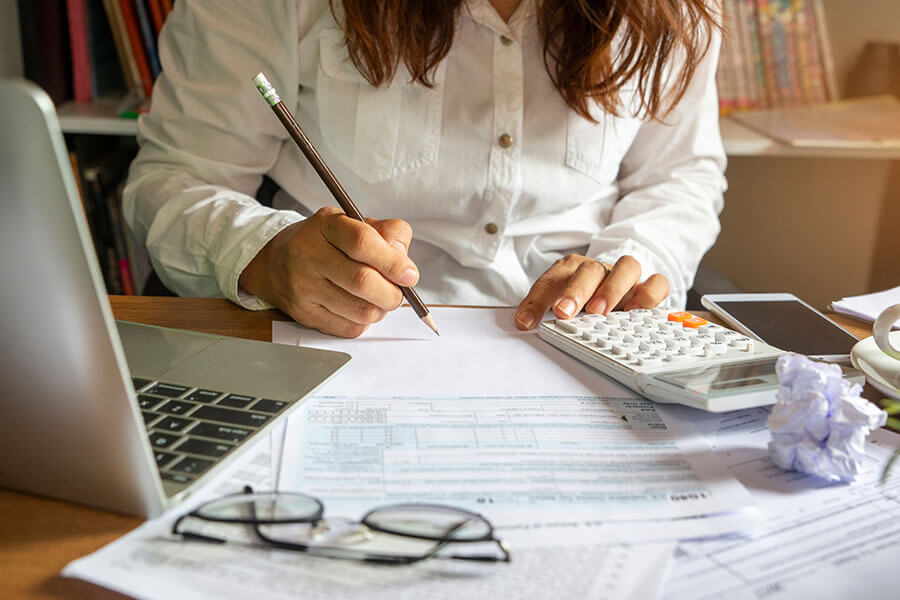 A person writing on document with laptop and calculator nearby