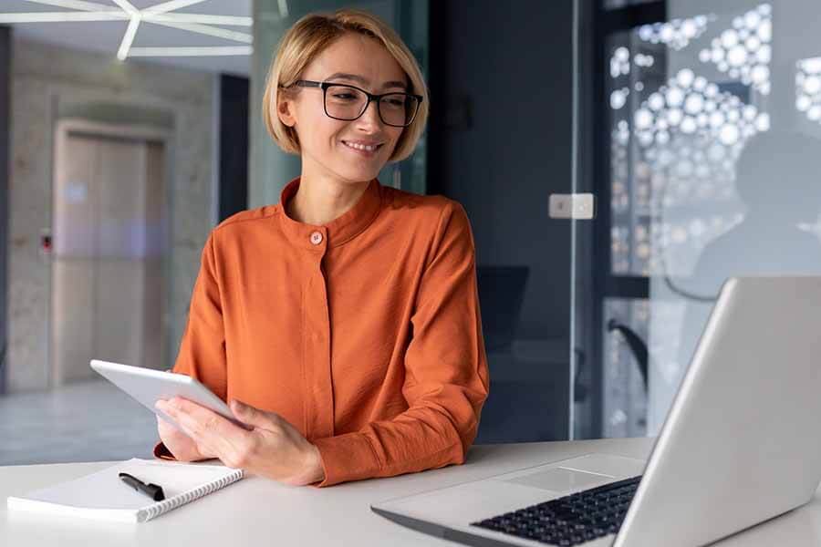 A person smiling at laptop holding a ipad