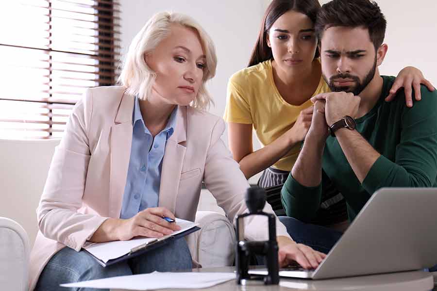 Three people gathered around computer looking at screen with worried expressions.