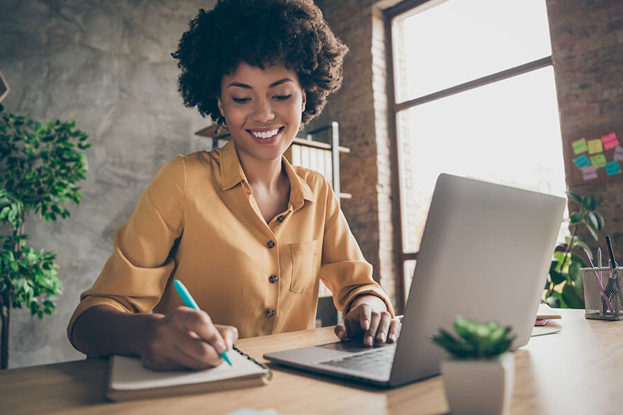 A person writing on a document with a laptop