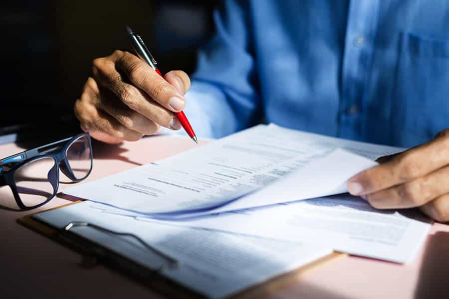 A person holding a pen with documents on the desk