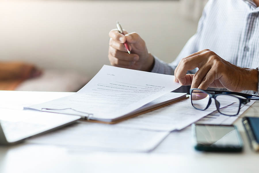 A person holding a pen while reviewing documents at a desk with papers.
