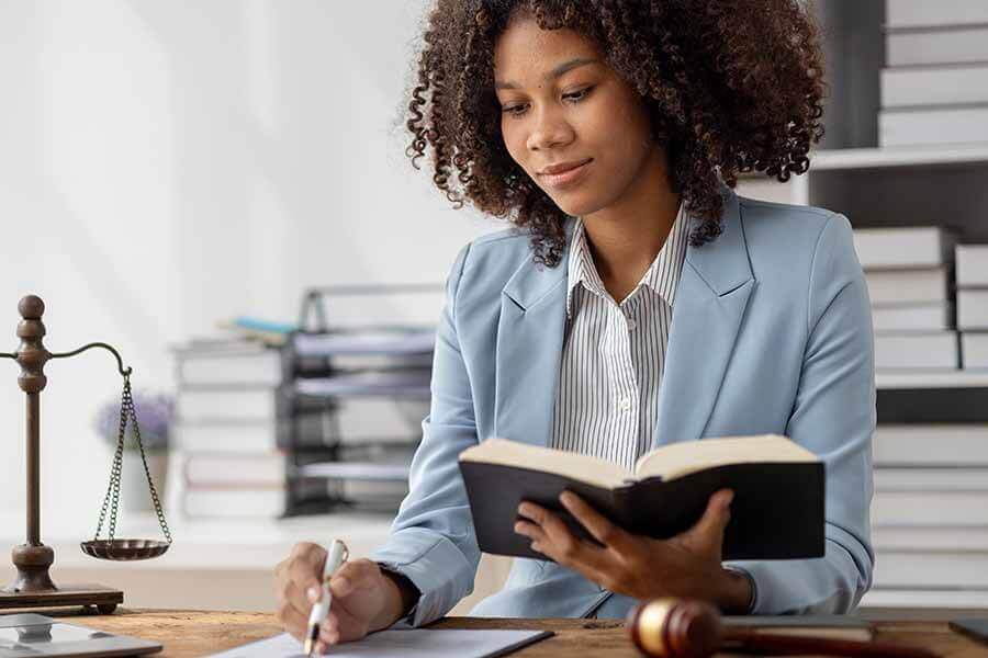 A person writing on document while holding open book in other hand.