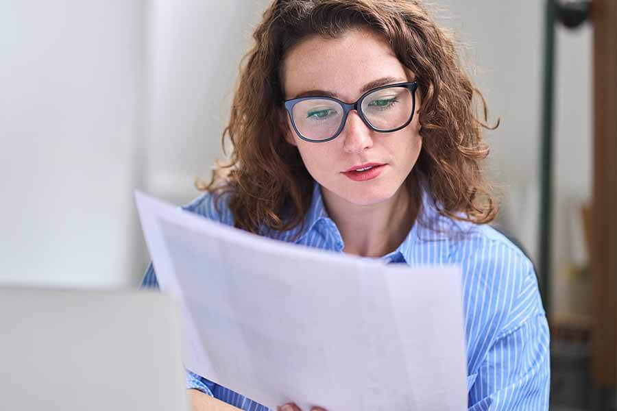 Person reading a document at a desk, wearing glasses and looking focused.