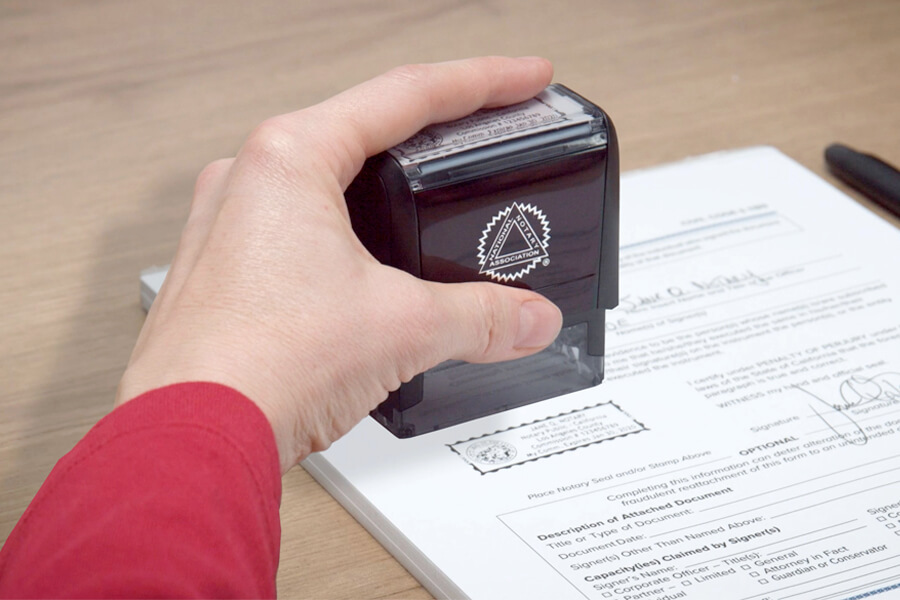 A hand holding an ink stamp, with the stamped impression visible on a document