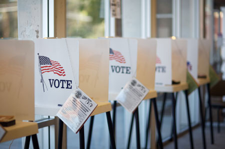 A row of voting booths with American flags and VOTE signs visible.