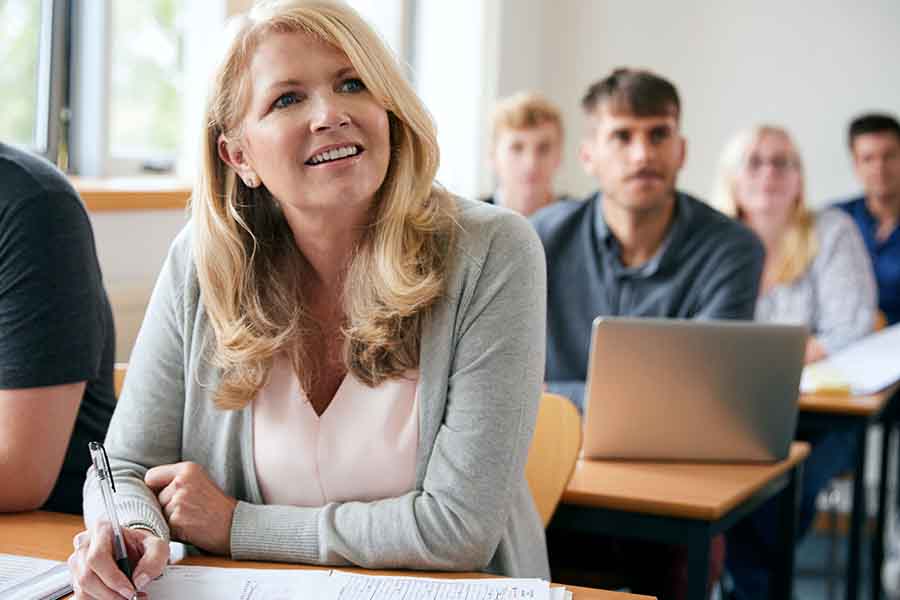 Full classroom with a smiling person at a desk facing the front.