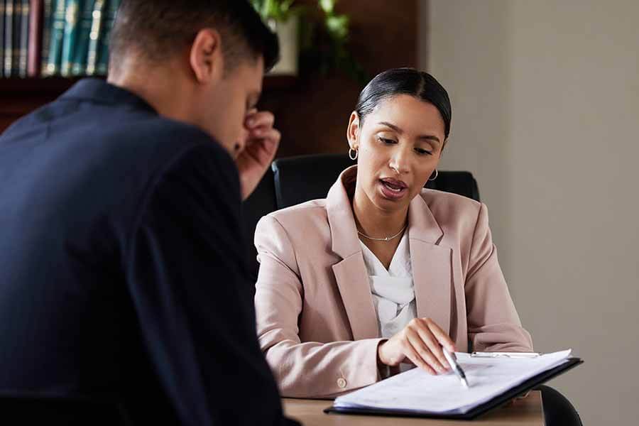 Two people discuss a document at a table, with one person explaining while the other listens.