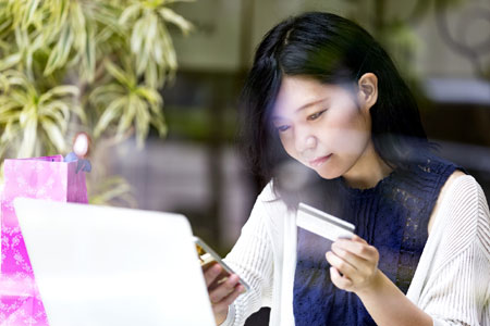 Woman looking at an ID and phone in front of a laptop