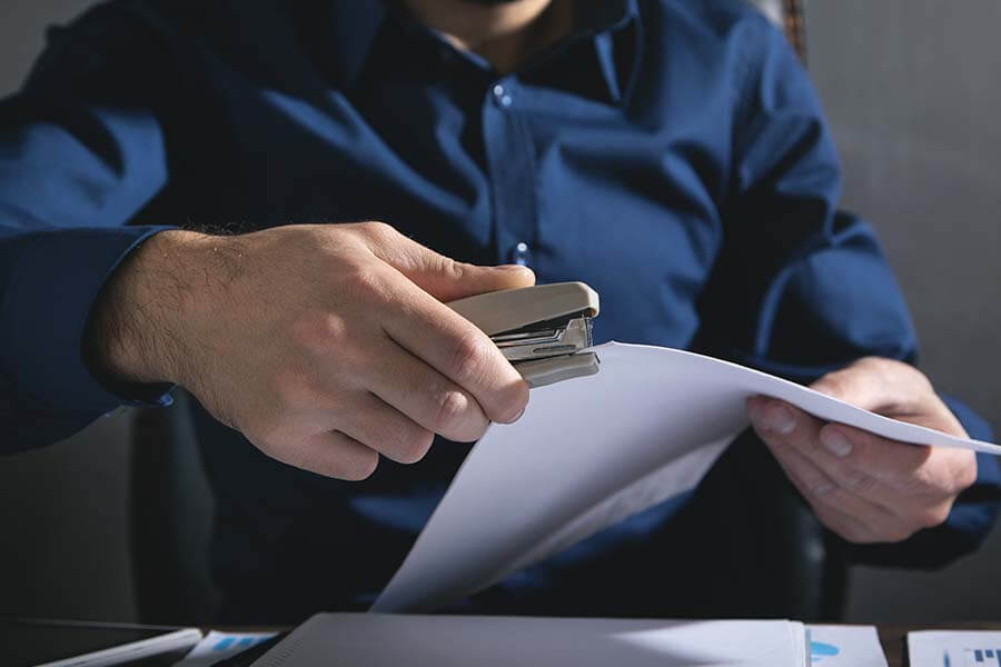 A person using a stapler on white sheets of paper.