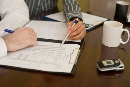 One hand with a pen pointing to a section of a document