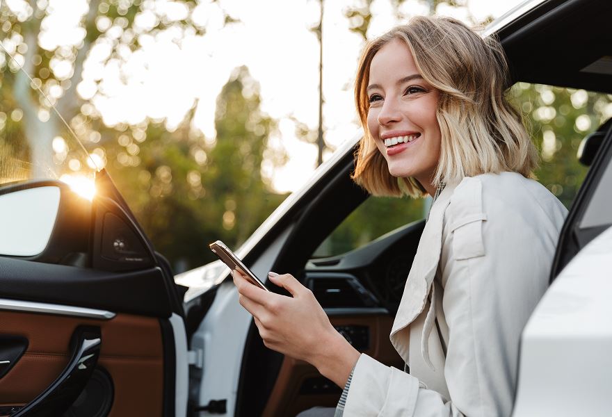 Woman smiling while sitting in a car and holding a phone.