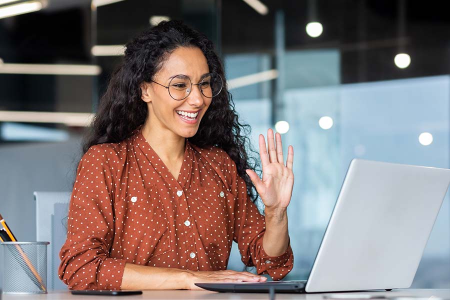 Smiling female Notary in glasses and orange blouse with her hand raised in front of a laptop