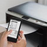 Hand holding a smartphone above a portable printer.