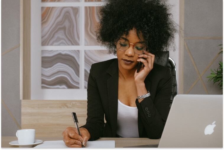 Woman in suit on the phone writing notes at her desk