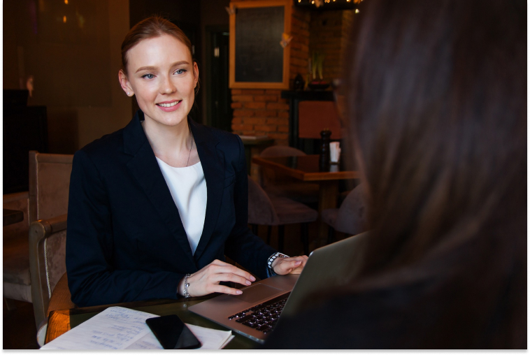 Woman in suit sitting in front of her laptop looking toward someone