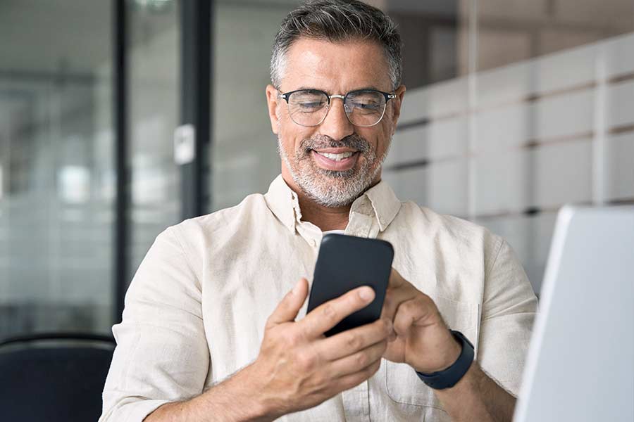 Smiling man seated at a desk looking down at his mobile device